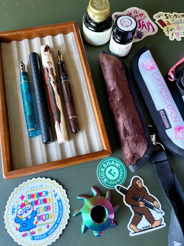 Here’s my PNW Pen Show stationery haul! In yesterday’s livestream, I talked about my experience at the @pnwpenshow (in Portland). Check out the replay on TW and YT - if you joined in the chat or are watching the replay, thank so much 🫶🏽  Highlights for me were hanging out with friends (new and seasoned) and sharing part of the pen show experience with my two daughters and husband. It was a small but intimate show and I enjoyed the time I got to spend there.  Featured in my haul:
- Oblation “Oregon Marionberry” PNW Pen Show ink (and “Oblation Olive”, standard ink line) + stickers and notepad
- Ink-a-pet ink vial holders
- Stickers and washi tape from The Washi Station
- Zodiac Pens (Capricorn model) fountain pen in “Caffeine Withdrawals” by Brooks.
- Schon DSGN for Gena of Custom Nib Studio fountain pen in Ultem (Perspective nib by Gena)
- Custom nib grind by Gena of Custom Nib Studio: Smooth Cursive Italic on a Sailor Pro Gear “Soda Pop” Music nib.
- Rickshaw Fillmore pen pouch in Doodle Cat White
- Rickshaw PNW Pen Show pen sleeve (brown fuzzy Sasquatch) gifted by Mark  #stationeryhaul #fountainpens #fountainpenink #rickshawbags #oblationpapers #pnwpenshow